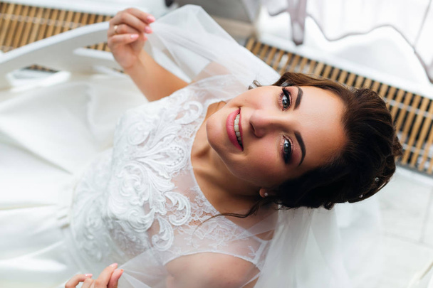 The bride is sitting on the chair and looking into the camera. b - Φωτογραφία, εικόνα