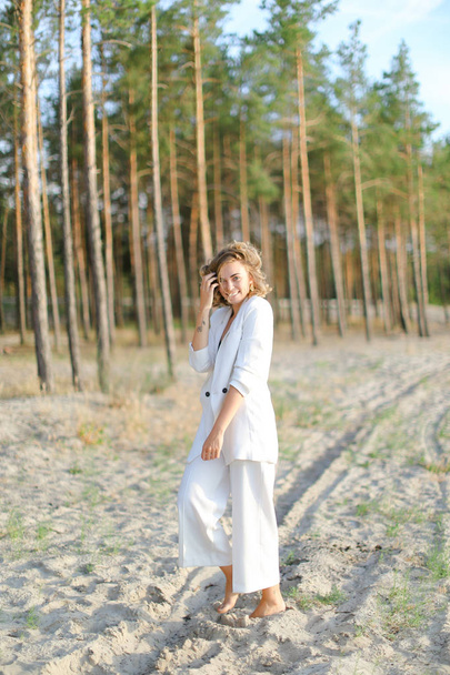 Sarışın güzel kadın kum plajda yürüyüş ve beyaz giysiler giyiyor. - Fotoğraf, Görsel