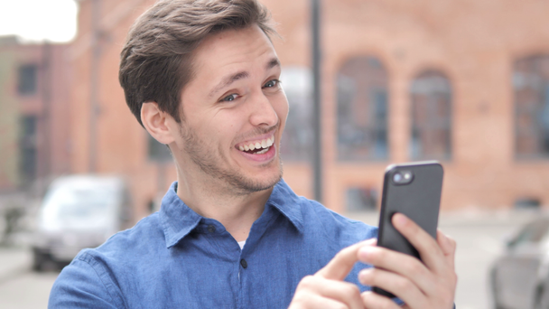 Vau, ulkona muotokuva yllättynyt nuori mies käyttää älypuhelinta
 - Materiaali, video