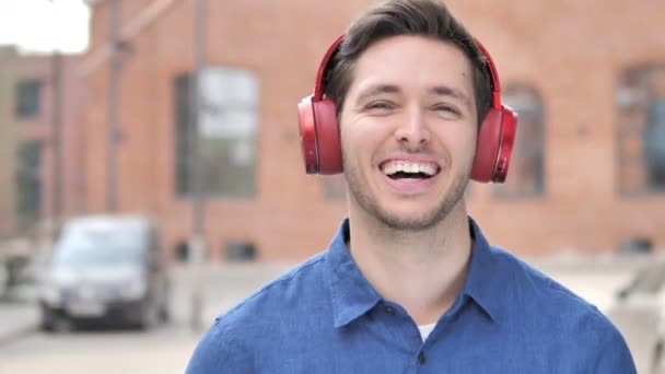 Odkryty młody człowiek słuchanie muzyki na czerwone słuchawki - Materiał filmowy, wideo