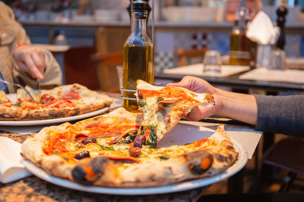 Nainen käsi ottaen viipaleita maukasta pizzaa lautaselta ravintolassa
. - Valokuva, kuva