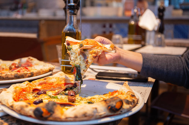 Ženská ruka s plátky chutných pizz z talíře v restauraci. - Fotografie, Obrázek