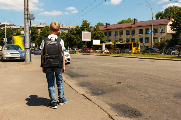 young schoolboy with a backpack waiting for the bus at the bus stop on the street of the city, hot summer day. Pupil of a middle school on his way home after the studying - Foto, immagini