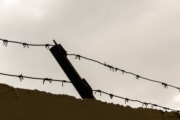 Ogrodzenia z drutu kolczowego na szarym niebie. symbol przedstawiający uwięzienie w więzieniu - Zdjęcie, obraz
