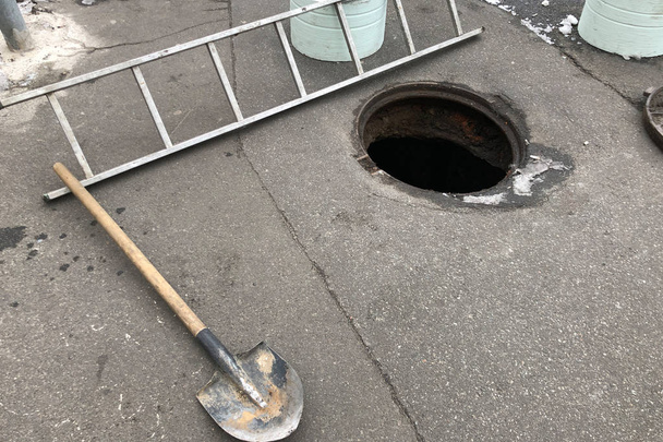 opened manhole in the asphalt with Ladder, Shovel and iron hatches and metal fencing - Photo, Image