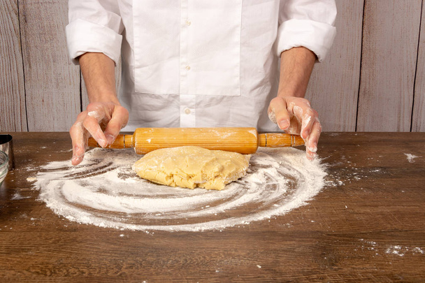 Preparación de masa para galletas, pasteles, pasteles, pizza. Las manos despliegan la masa con un rodillo sobre una mesa de madera, en el primer plano de la cocina. Copiar espacio, espacio para texto
 - Foto, Imagen