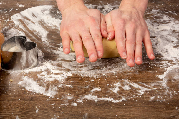 Příprava těsta na sušenky, koláče, koláče, pizzy. Ruce se hnětou na dřevěné stolek v kuchyňském plášti. Kopírovat mezeru, prostor pro text - Fotografie, Obrázek