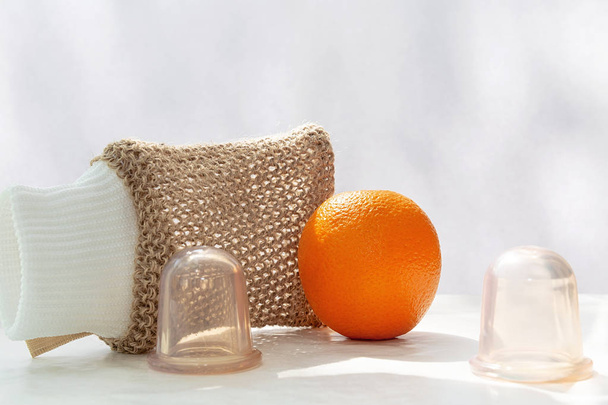 Une orange est sur la table et à côté se trouvent des canettes sous vide et un gant de toilette en maille fabriqué à partir de fibres naturelles.
. - Photo, image