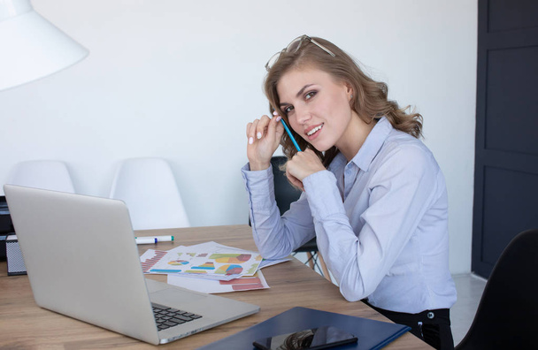 Concentrated young beautiful businesswoman working on laptop in bright modern office - Фото, изображение