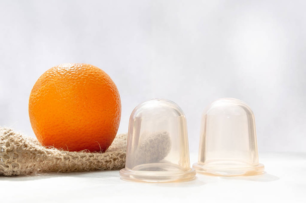 The orange lies on a mesh washcloth made from natural fibers, and next to it are vacuum banks. - Photo, Image