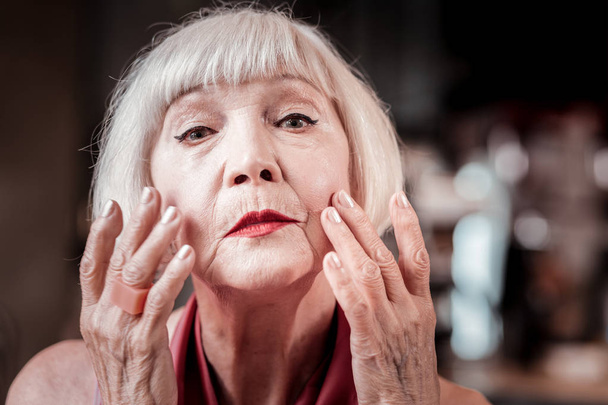 Gentle blonde senior lady covering skin on her face - Zdjęcie, obraz