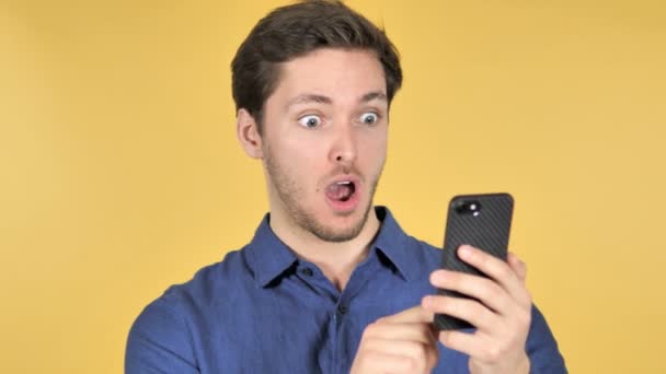 Wow, zaskoczony casual młody człowiek za pomocą smartfona na żółtym tle - Materiał filmowy, wideo