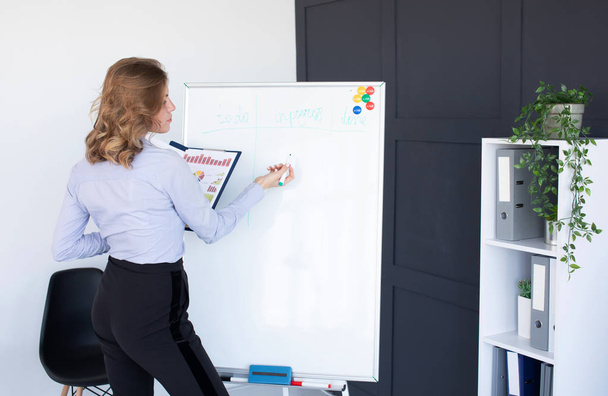 Young woman in an office writing on a whiteboard, close up - Foto, afbeelding