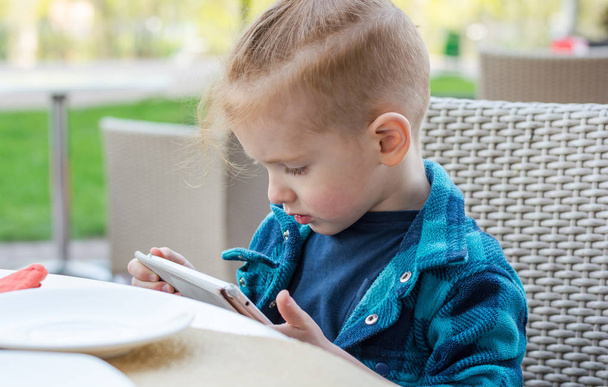 Portrait of a cute little boy who playing on a tablet in a cafe - Foto, Imagen