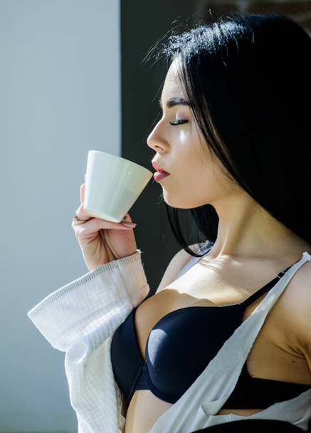 Sip of creamy cappuccino. Morning ritual. Girl sexy breasts drinking coffee near windowsill. Attractive female lingerie relaxing at home. Perfect coffee time. But first coffee. Tranquility and peace - Fotografie, Obrázek
