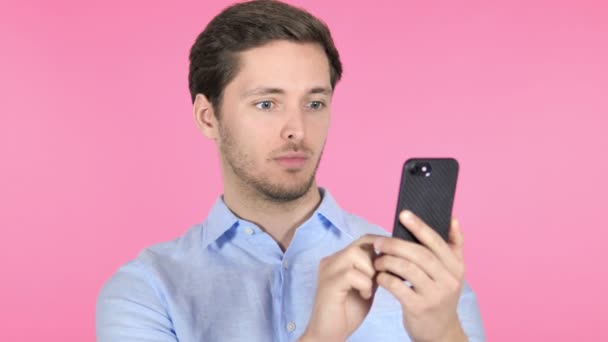 Wow, έκπληκτος νέος άνθρωπος χρησιμοποιώντας smartphone σε ροζ φόντο - Πλάνα, βίντεο