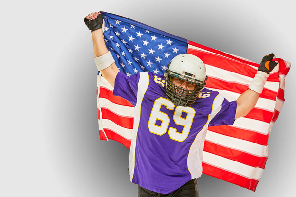 jugador de fútbol americano con uniforme y bandera americana orgulloso de su país, sobre un fondo blanco
. - Foto, Imagen