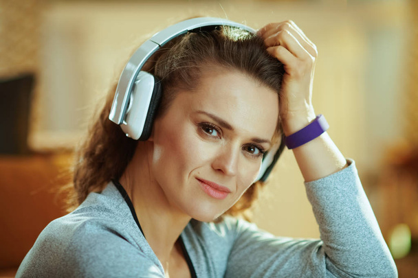Portrait of happy young woman in sport clothes listening to the music with headphones in the modern house. - Фото, зображення