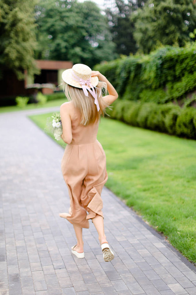 Rückseite der jungen blonden weiblichen Person in körperfarbenen Overalls und Hut mit Blumen. - Foto, Bild