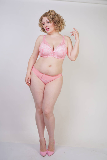 Mulher gordinha muito caucasiana com corpo plus size e pele pálida vestindo roupa interior sexy de renda rosa no fundo do estúdio branco isolado
 - Foto, Imagem