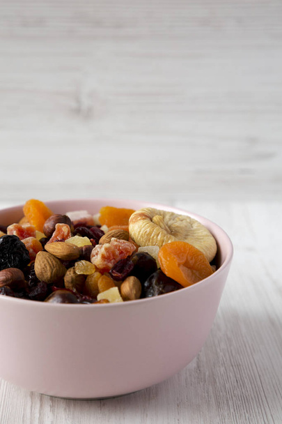 Sušené ovoce a ořechy v růžové misce nad bílým dřevěným backgronem - Fotografie, Obrázek