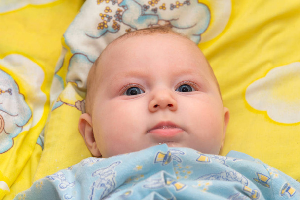 Vastasyntynyt vauva makaa vauvan sängyssä keltaisella taustalla ja hymyilee, lähikuva
. - Valokuva, kuva