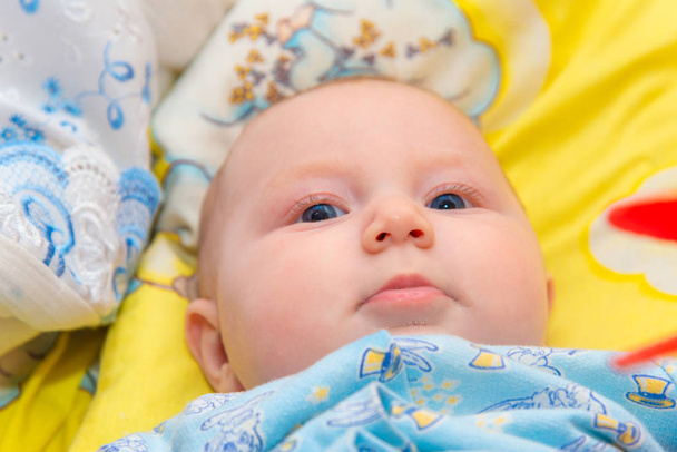 Newborn baby is lying in the baby bed on a yellow background and smiling, close-up. - Photo, Image
