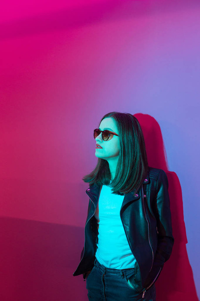 Fashioned girl in leather jacket in dark glasses in pink anf blue  neon lights background.  - Foto, immagini