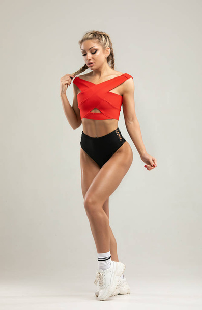 Happy young woman in sports clothing. Muscular fitness model on grey background. Red and black clothes. - Foto, immagini