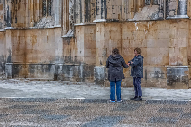 Вид на туристов, говорящих на внешней стороне рядом с готическим внешним фасадом монастыря Баталья, Мостейро да Баталья, буквально монастырь битвы, является доминиканский монастырь, в Лейрии, Пор
 - Фото, изображение
