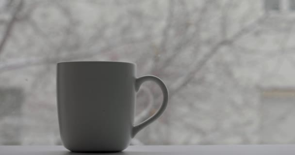 Κύπελλο με ένα ζεστό ποτό και χιόνι πέφτει - Πλάνα, βίντεο