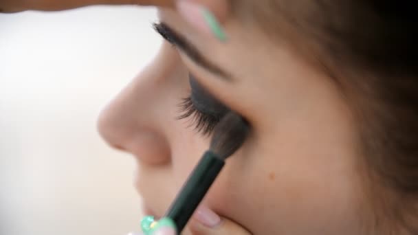 Hands make-up artist applied makeup on the face of a young woman. Girl doing eye makeup in a professional salon. Evening makeup. Smokey eyes. 4k - Filmagem, Vídeo