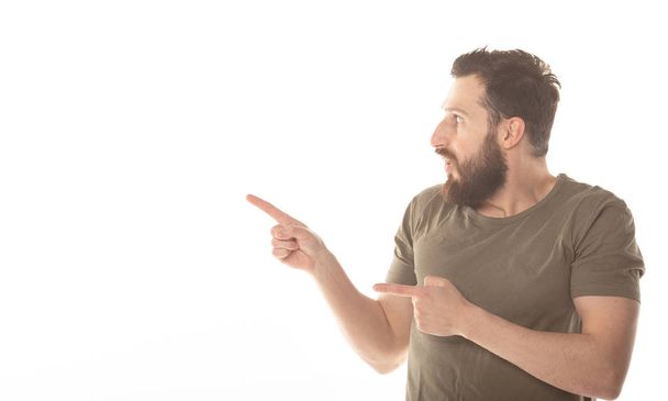 Surprised happy bearded man in shirt pointing away and looking at the camera over white background. - Foto, Bild
