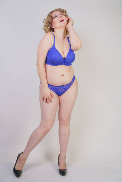 Pretty caucasian chubby woman with plus size body and pale skin wearing blue lace sexy underwear and high heels on white studio background - Photo, Image