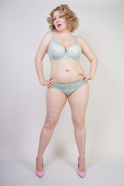 Pretty caucasian chubby woman with plus size body and pale skin wearing green lace sexy underwear on white studio background - Фото, изображение