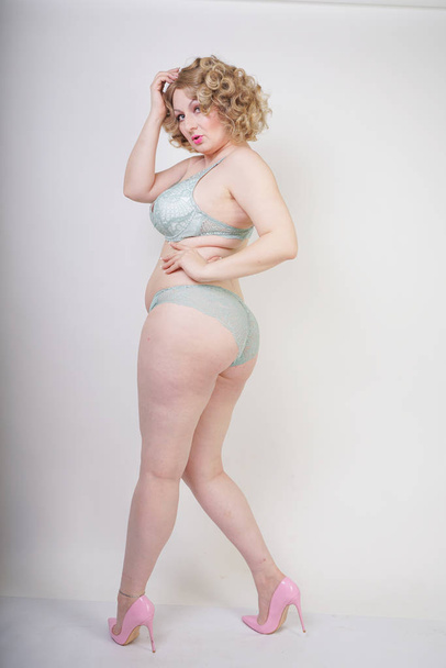 Pretty caucasian chubby woman with plus size body and pale skin wearing green lace sexy underwear on white studio background - Zdjęcie, obraz