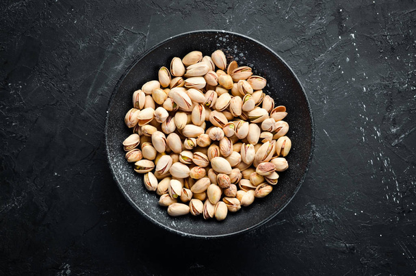 Salt pistachios in a bowl on a black background. Top view. Free space for your text. - Foto, Imagen