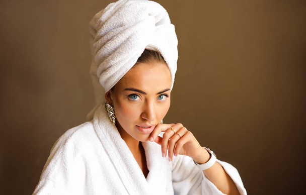 Beauty portrait of young pretty lady with blue eyes and big lips. Accessories on the hand, watches and earings. Towel on the head, natural makeup on the face. Wearing white hotel bathrobe. - Zdjęcie, obraz