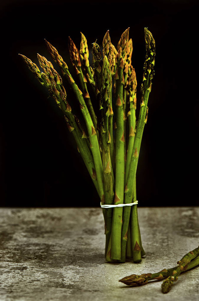 Bunch of fresh asparagus on a concrete base and a black background. - Foto, Bild