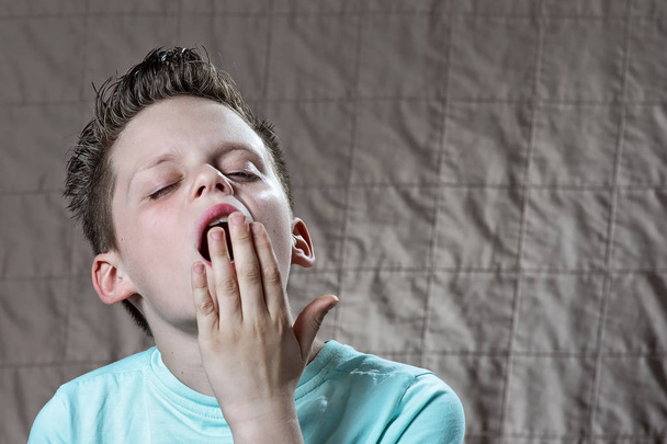 the boy in the t-shirt is tired, wants to sleep and yawns - Foto, afbeelding