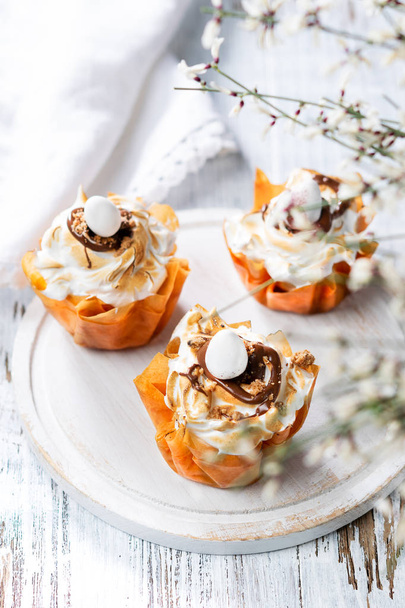 Fancy Phyllo dough cups with meringue and melted chocolate close up on a plate. White rustic background with space for your text. - Φωτογραφία, εικόνα