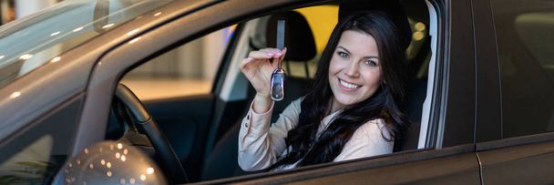 Happy woman buyer examines her new vehicle in car dealership - Foto, Imagen