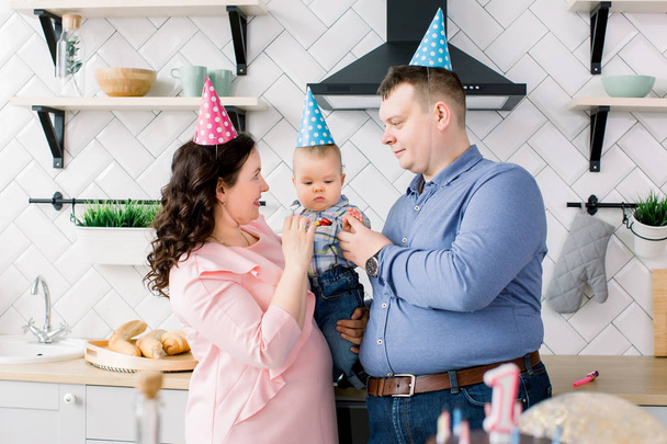happy little baby boy, father and mother with trumpets and balloons on birthday party. Young family celebrating birthday with a cake - Foto, Bild