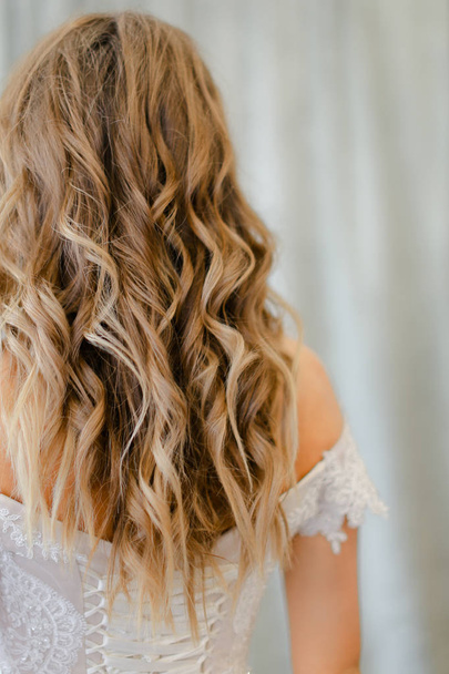 Πίσω όψη της νύφης με μακριά ξανθά σγουρά μαλλιά στο φωτογραφικό στούντιο. - Φωτογραφία, εικόνα