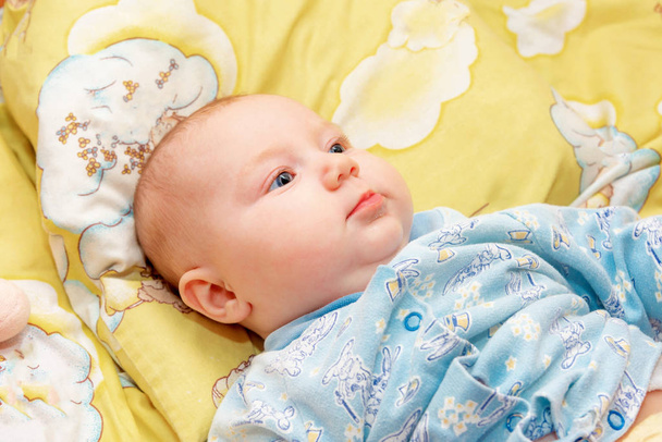 生まれたばかりの赤ちゃんは黄色の背景に赤ちゃんのベッドに横たわっていて、笑顔でクローズアップ. - 写真・画像
