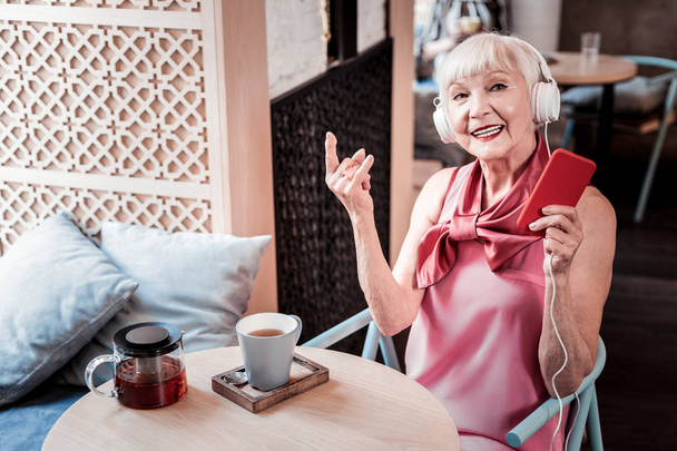 Stylish short-haired old lady in pink outfit showing rock gesture - Foto, Imagem