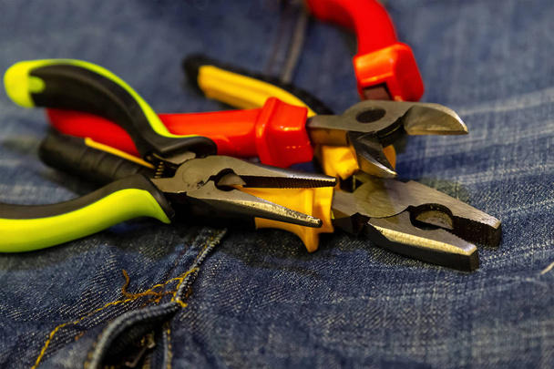 three wire cutters bright plastic green handles red yellow on jeans background close-up tools - Photo, Image