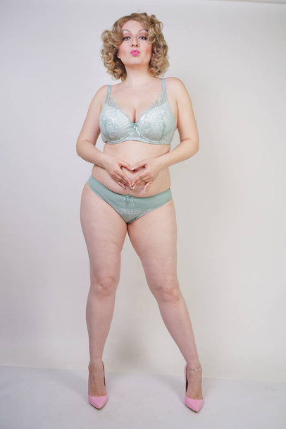 Mulher adulta com excesso de peso fica em lingerie e ama sua barriga e gordura em um fundo branco no estúdio. menina é harmoniosa e natural, amo-me conceito
. - Foto, Imagem