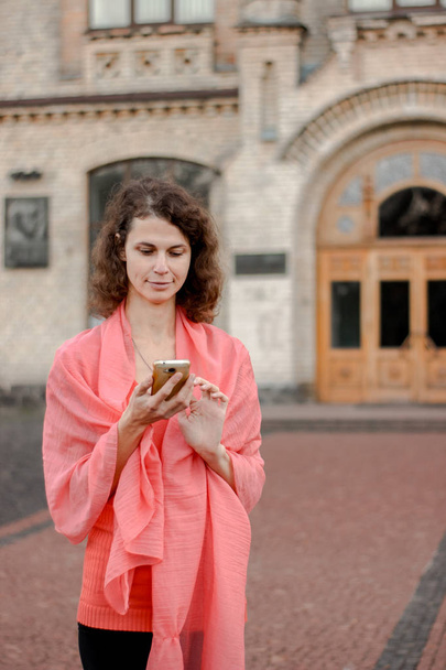 Μια γυναίκα κοιτάζει στο τηλέφωνο ενώ στέκεται δίπλα στο Πανεπιστήμιο - Φωτογραφία, εικόνα