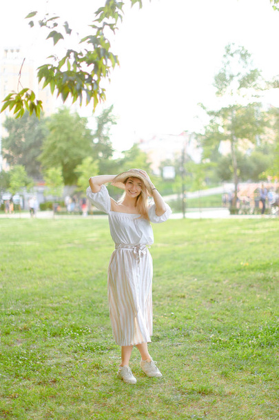 Young caucasian girl wearing hat and dress, standing in park. - Valokuva, kuva